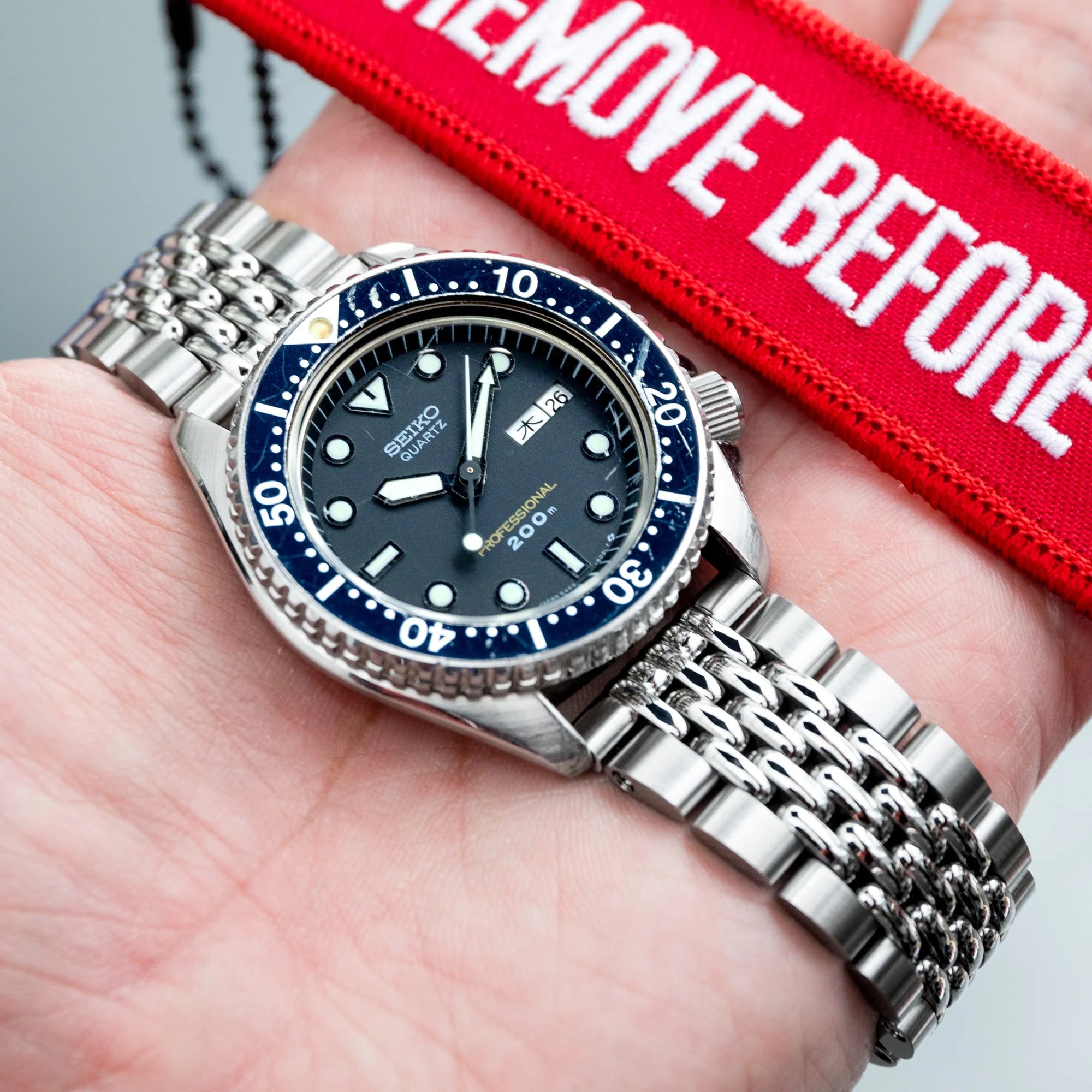 Seiko Prospex professional diver watch with blue bezel and steel bracelet on wrist, holding red equipment bag