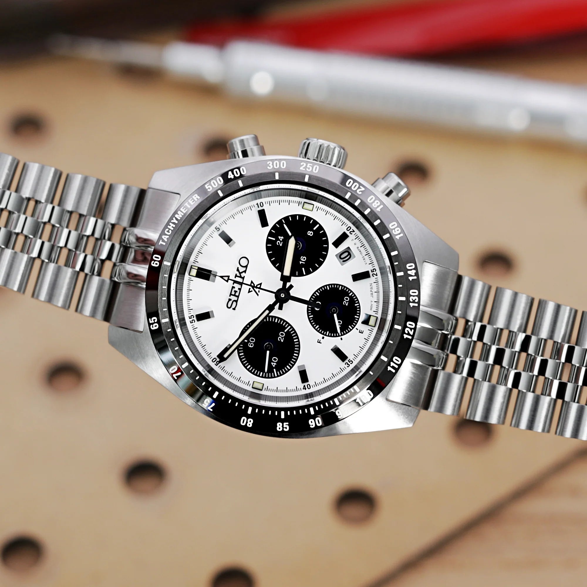 Seiko Speedtimer chronograph watch with white dial and three black subdials, stainless steel bracelet, tachymeter bezel on tan background