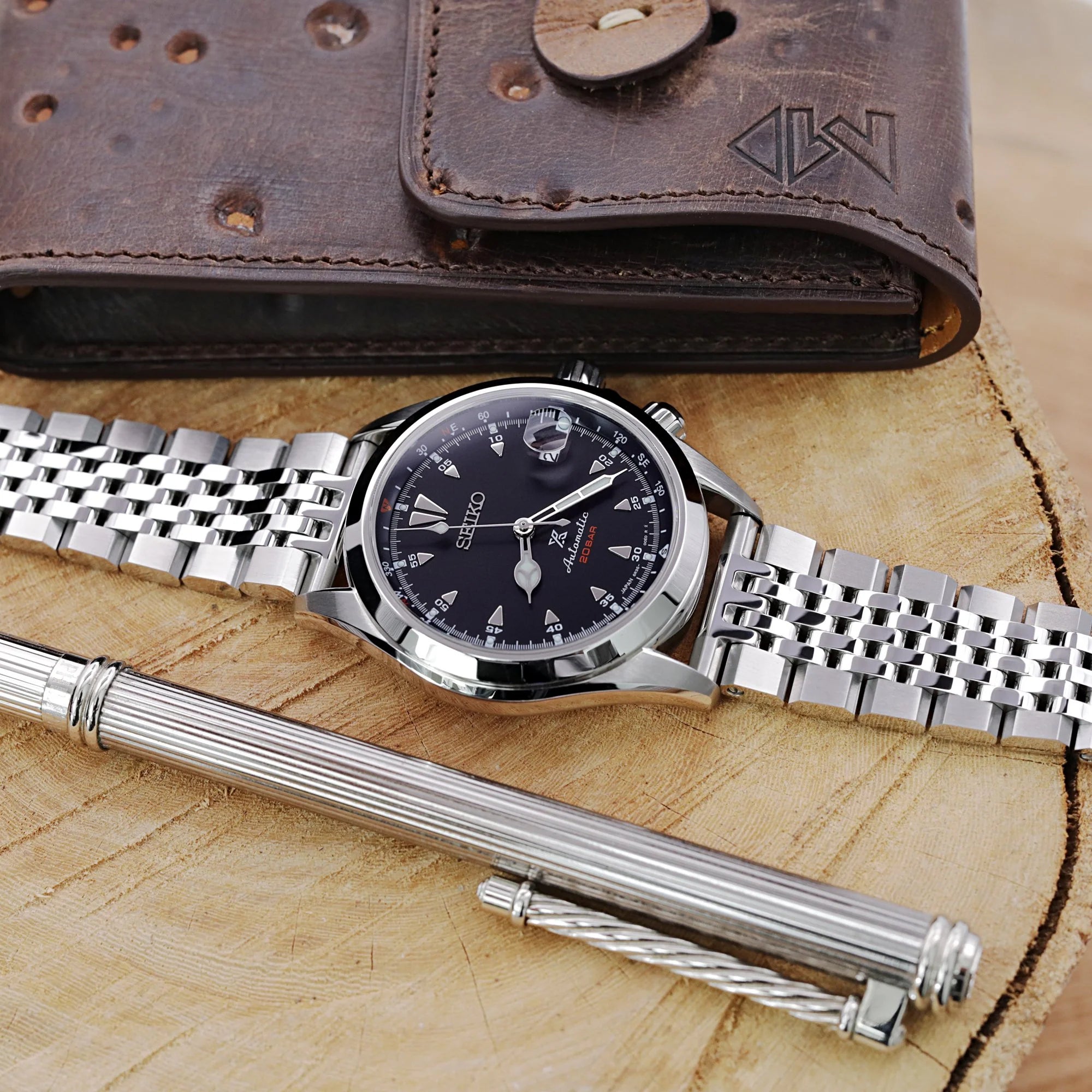 Strapcode Asteroid quick release watch bracelet with V-clasp in stainless steel, displayed with Seiko watch and leather accessories