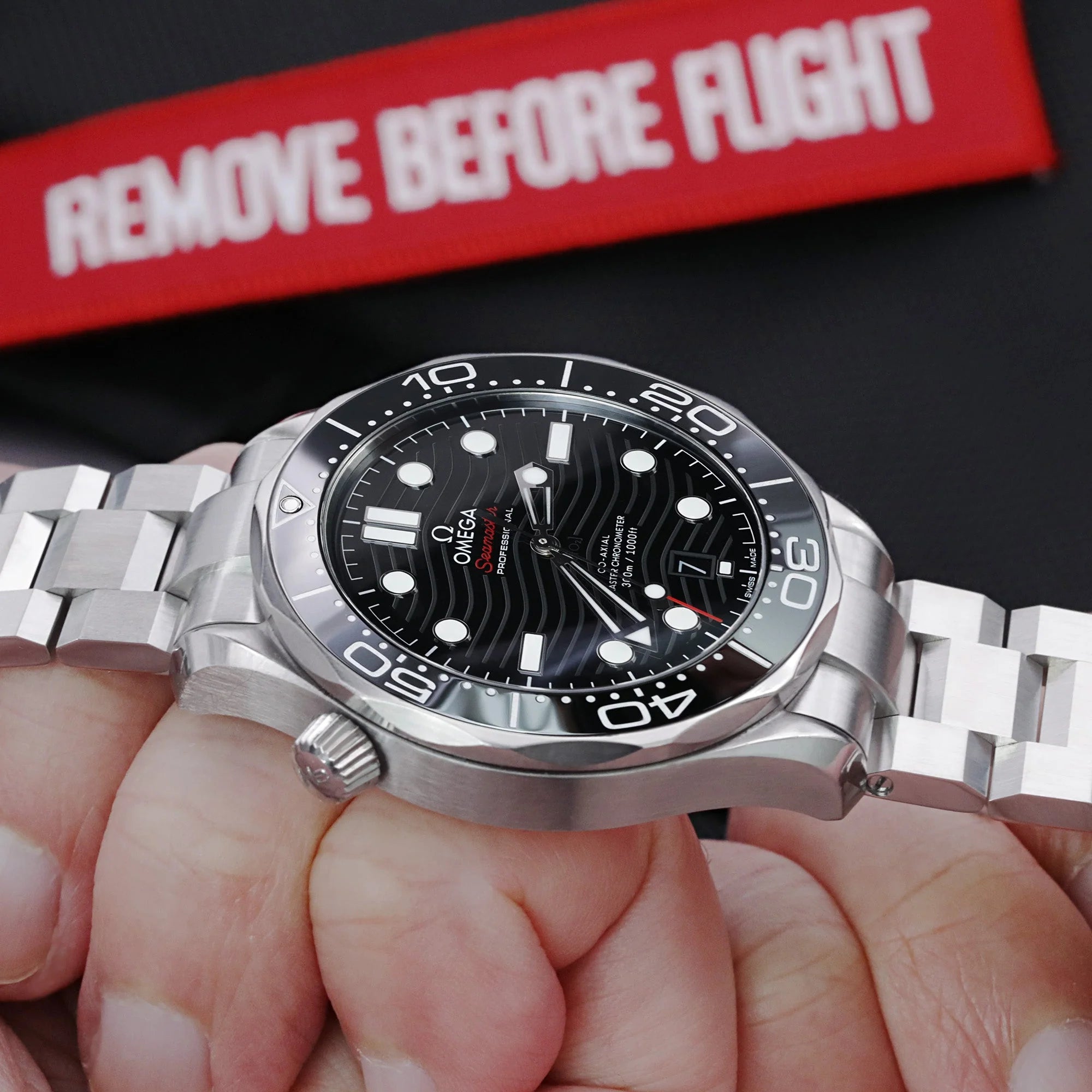 Omega Seamaster dive watch with black dial on stainless steel Hexad III bracelet, displayed in hand with red packaging