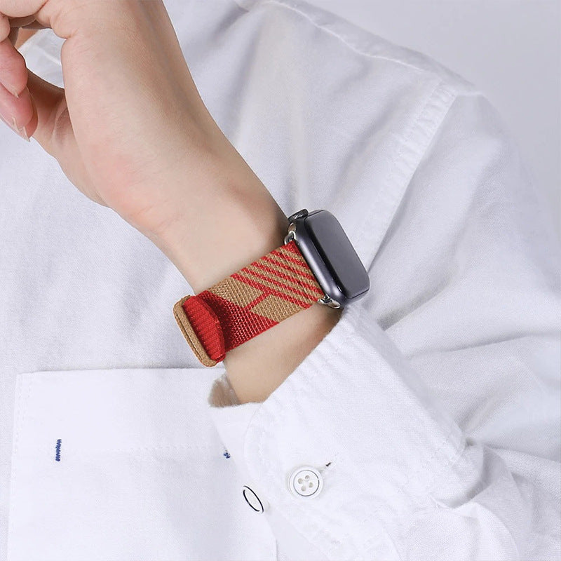 Red and tan woven fabric Apple Watch band with black connector on wrist, worn with white shirt sleeve