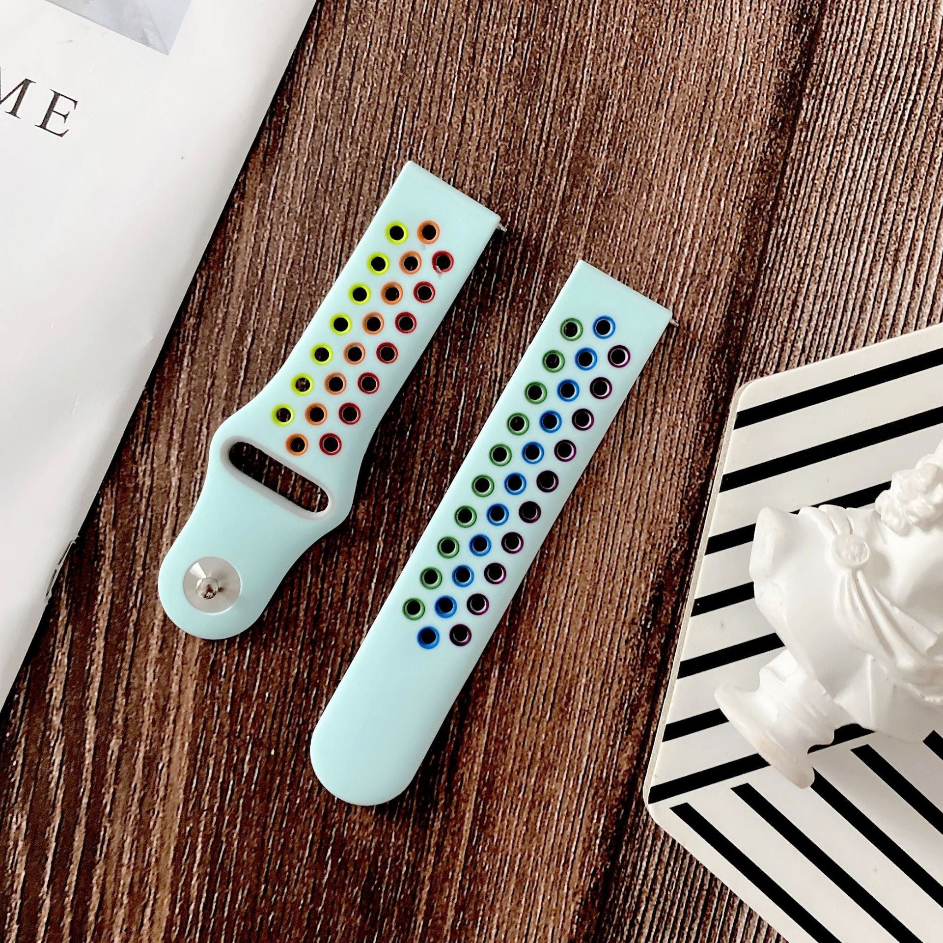 Light blue silicone smartwatch band with rainbow-colored sport studs and quick release connector on wooden surface