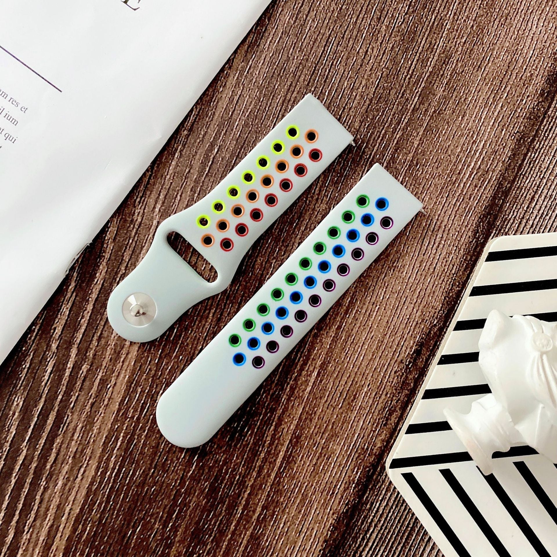 White silicone quick release sports strap with rainbow-colored snap buttons in green, blue, and orange tones on wooden surface