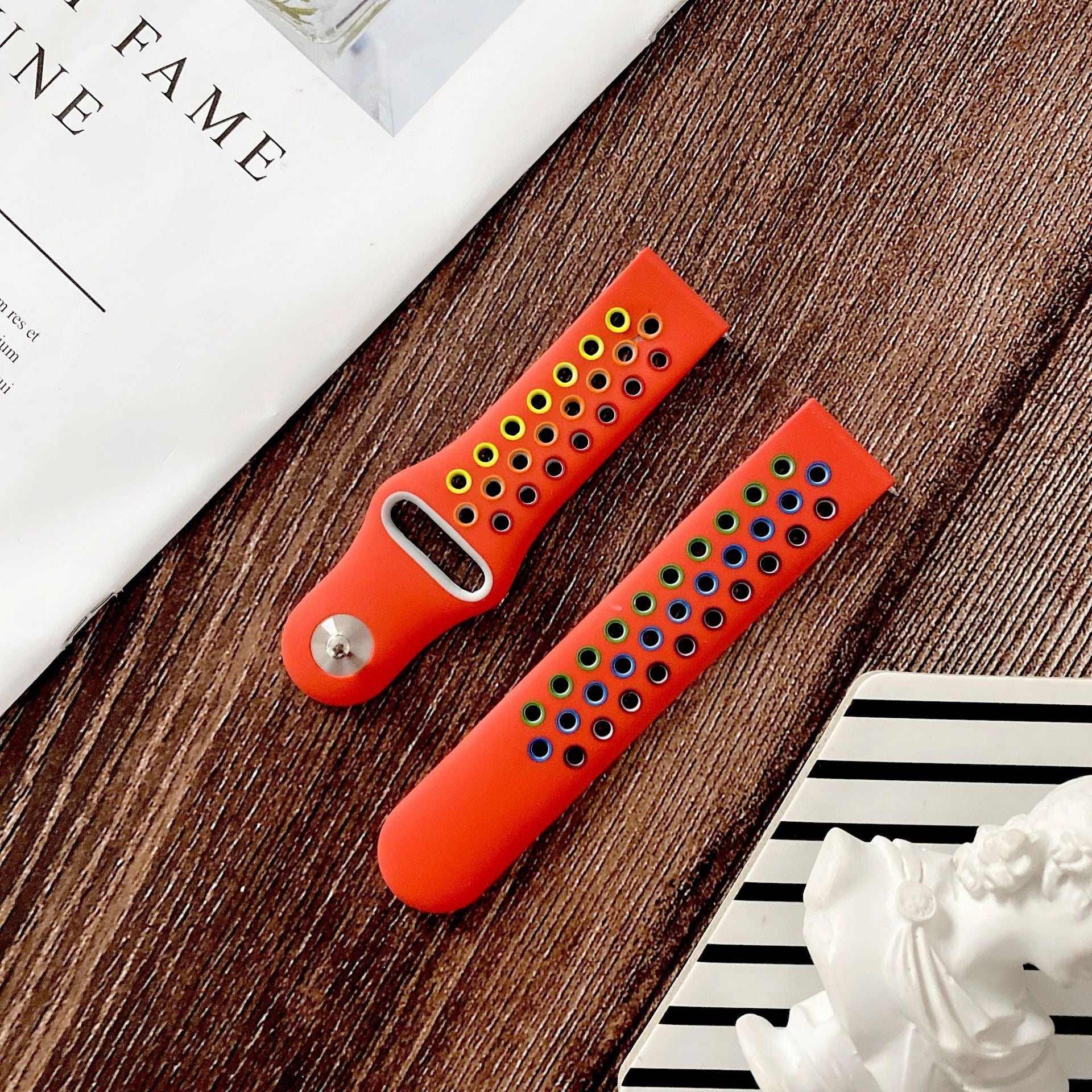 Bright red silicone smartwatch band with perforated ventilation holes and quick release connector, displayed on textured wood surface