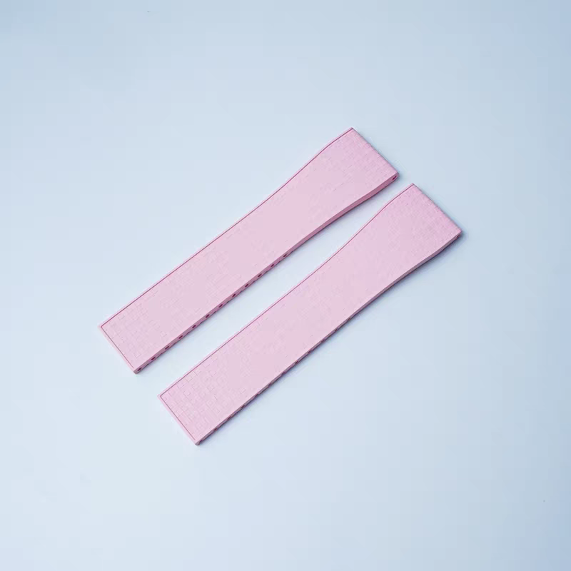 Two pink rubber watch straps with textured surface and leaf-spring deployant clasp hardware on light blue background