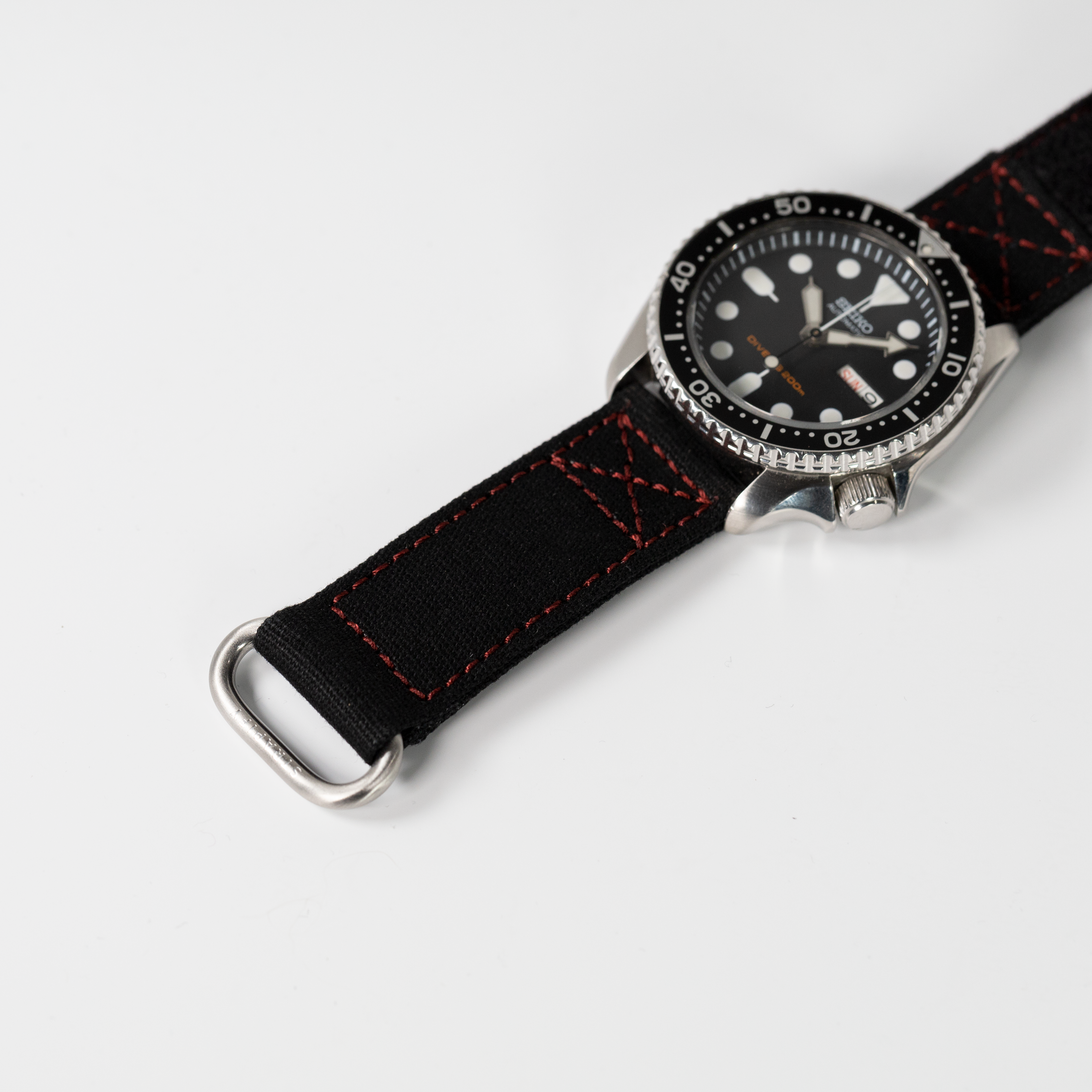 Military dive watch with black dial, rotating bezel, and quick release black fabric strap with red stitching
