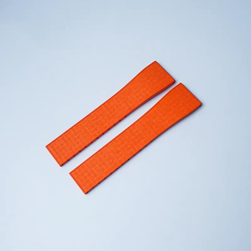 Pair of orange textured rubber watch straps with quick-release bars and deployant clasp mechanism on light blue background