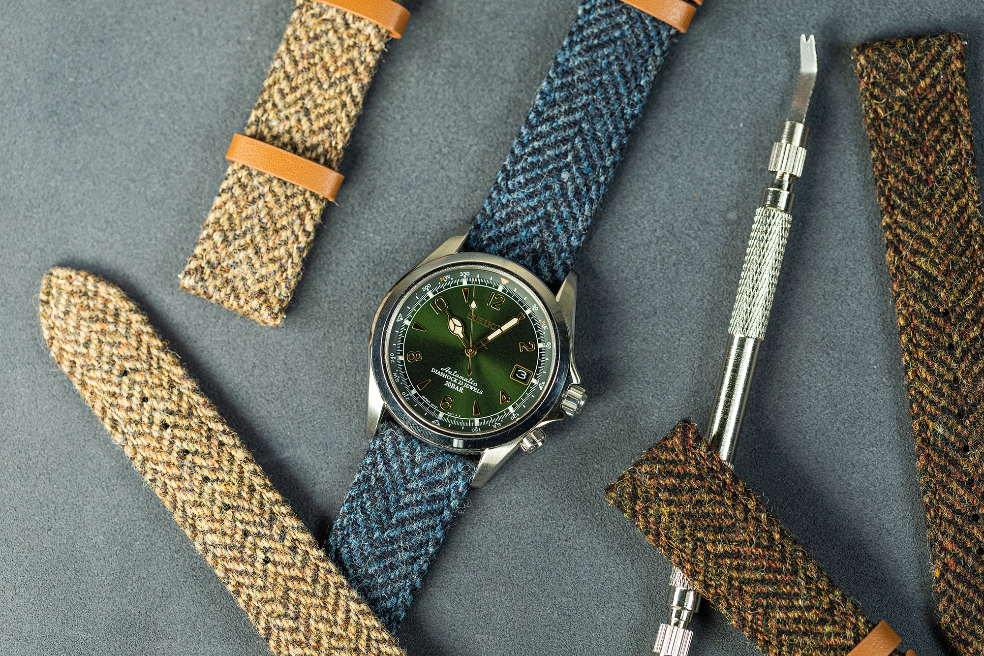 Luxury watch with green dial on dark blue Harris Tweed herringbone fabric strap with tan leather tabs and interchangeable straps