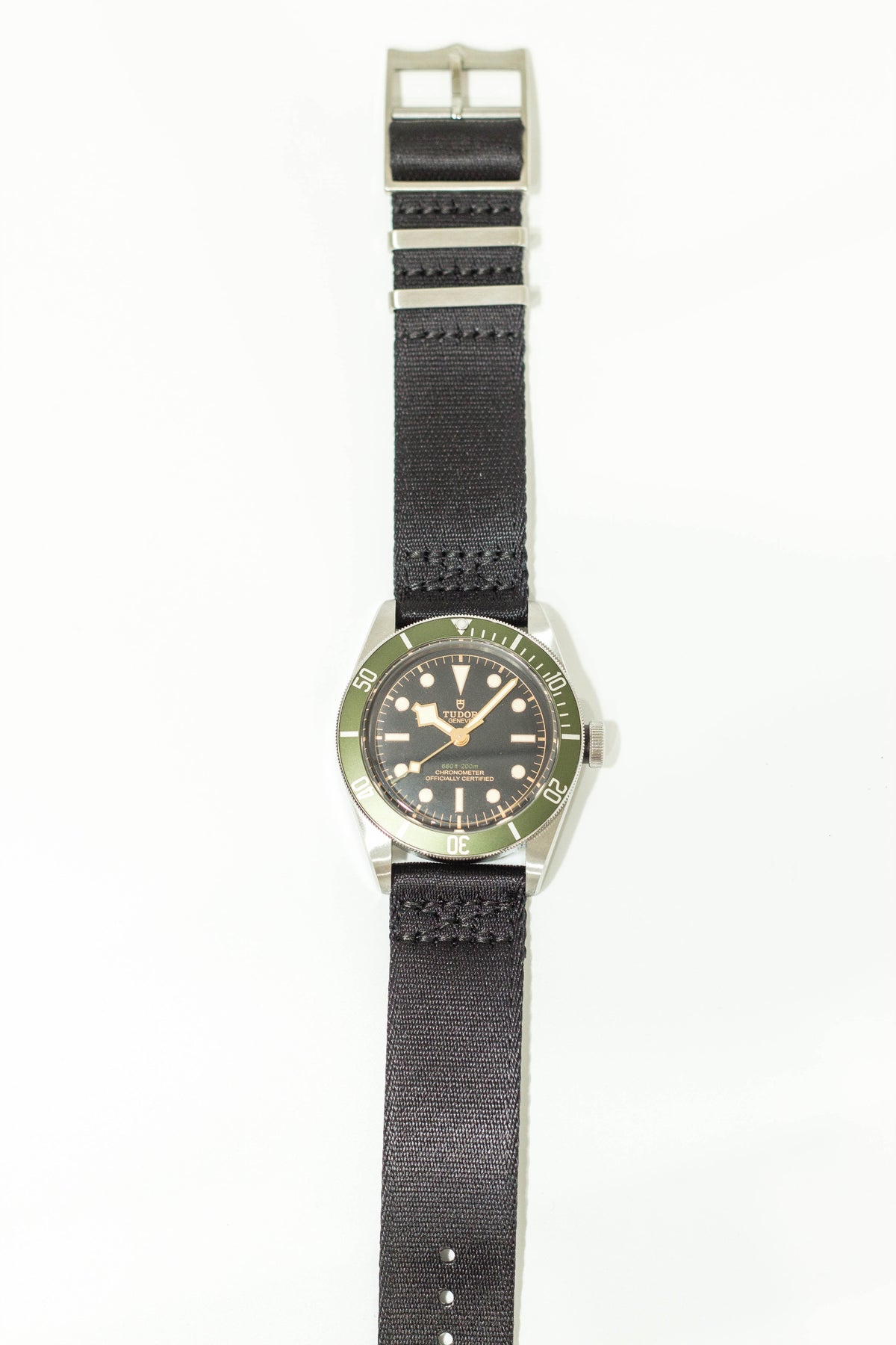 Tudor dive watch with green bezel, black dial, and black fabric strap with quick release buckle
