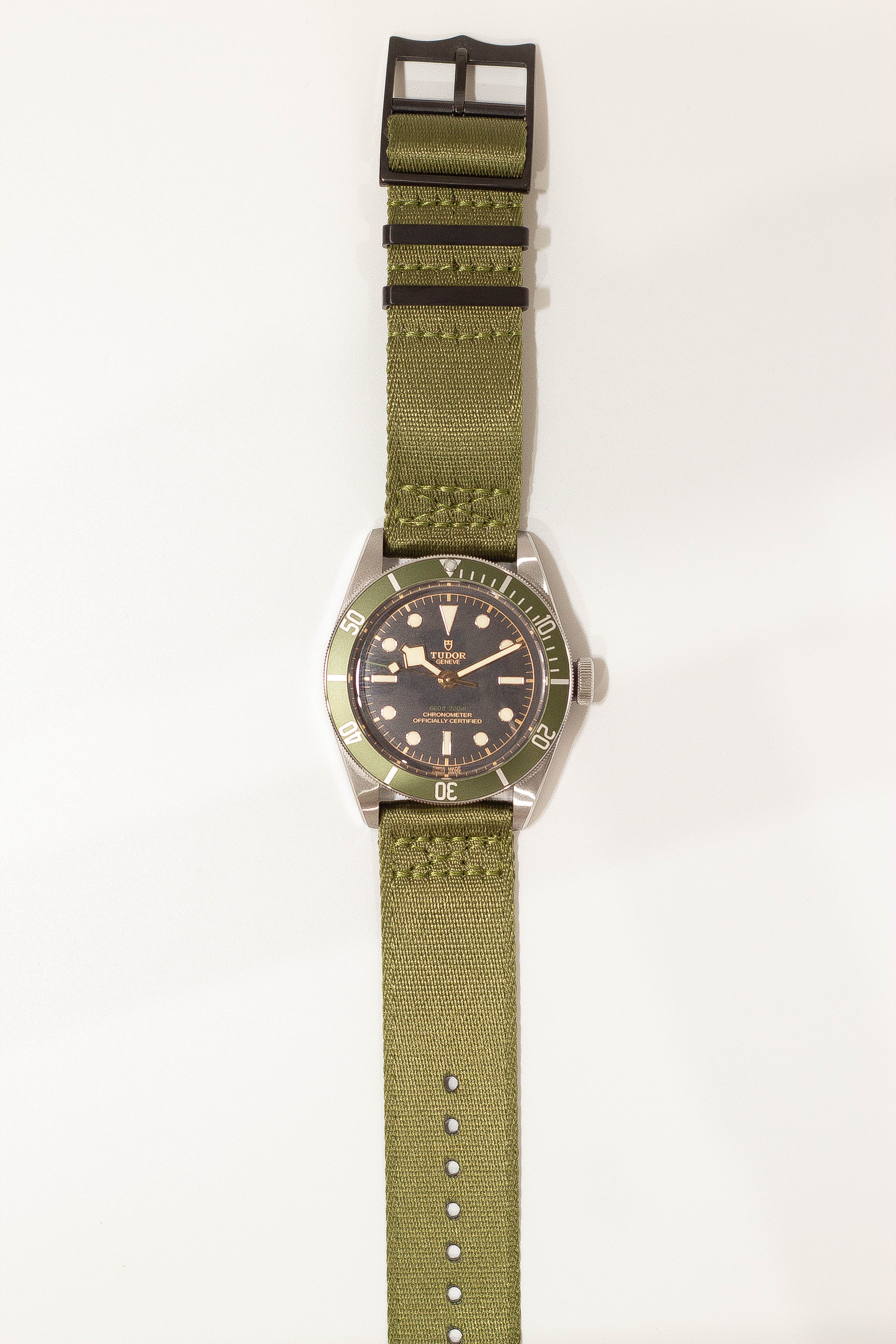 Tudor Black Bay dive watch with green fabric strap and black hardware, featuring dark dial and rotating bezel