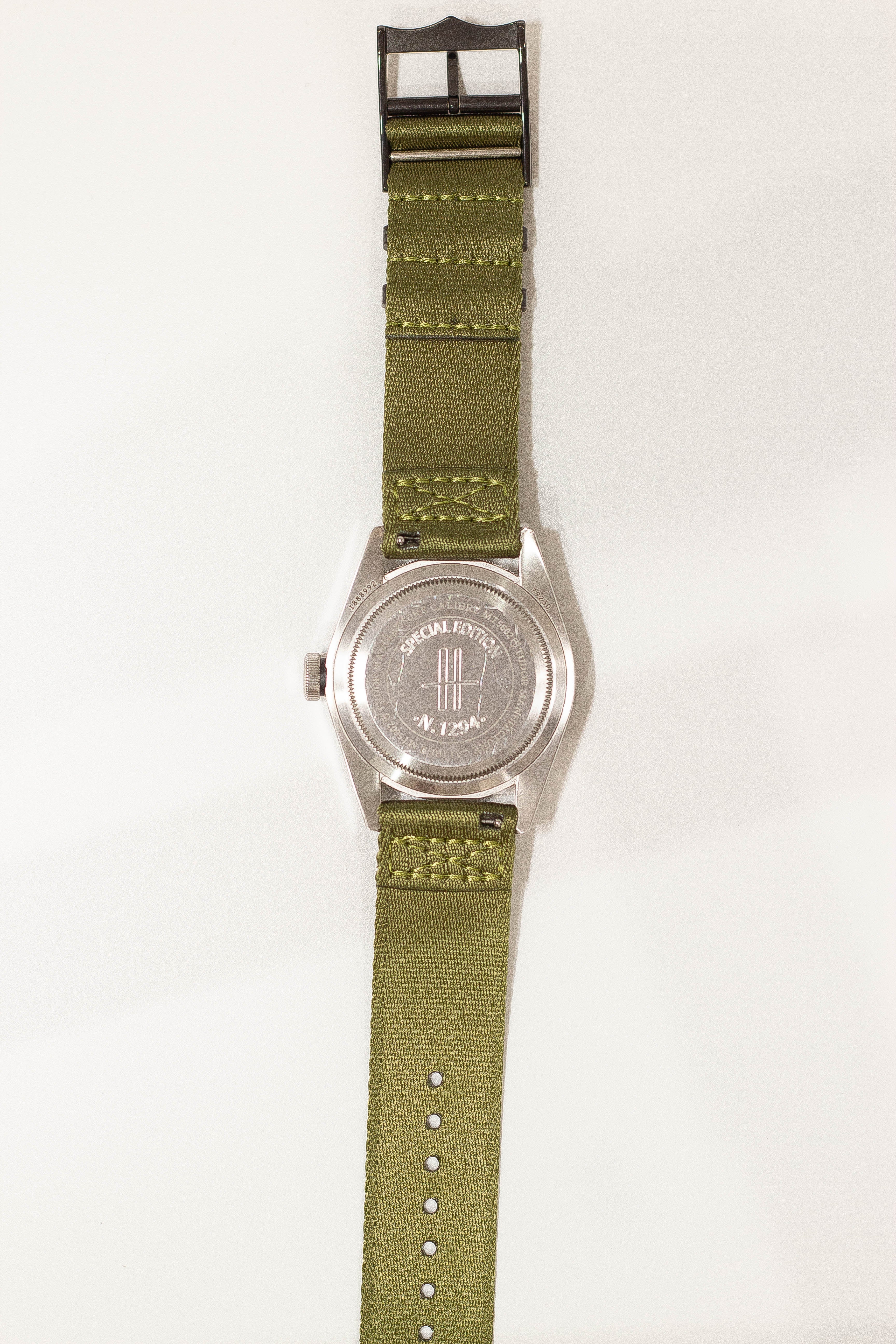 Special edition military watch with stainless steel case, olive green fabric strap, black hardware buckle, and engraved caseback