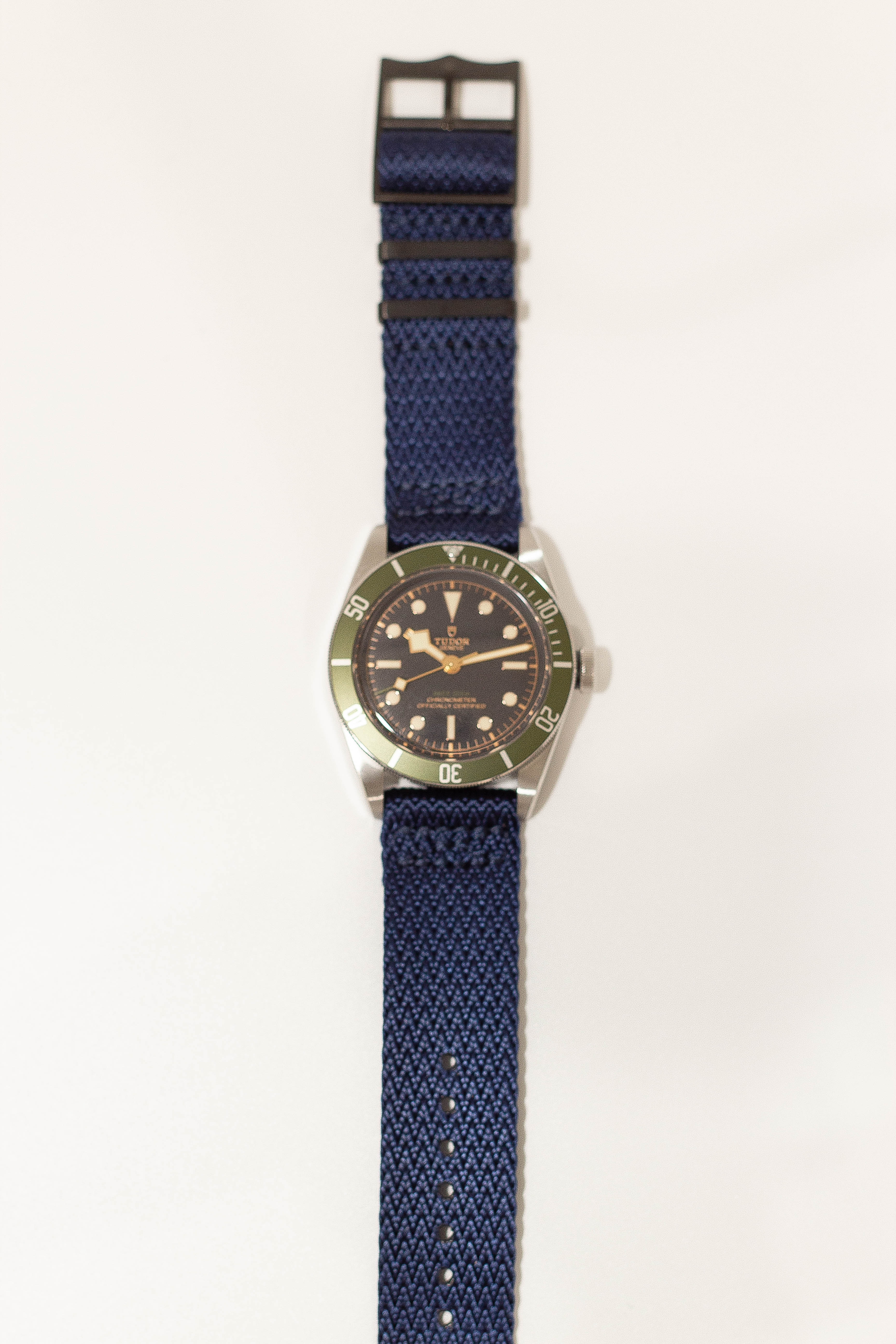Vintage Tudor dive watch with black dial, green bezel, stainless steel case, and navy blue fabric strap with black hardware