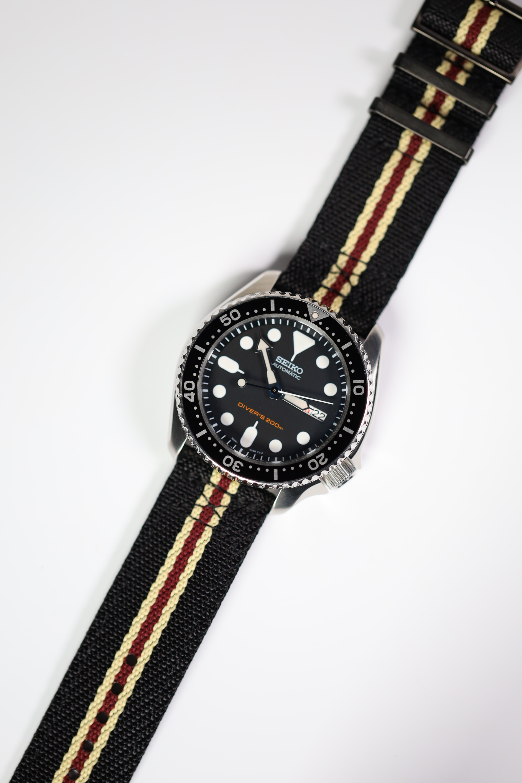 Seiko automatic dive watch with black dial and rotating bezel on black fabric strap with beige and maroon stripes and black hardware