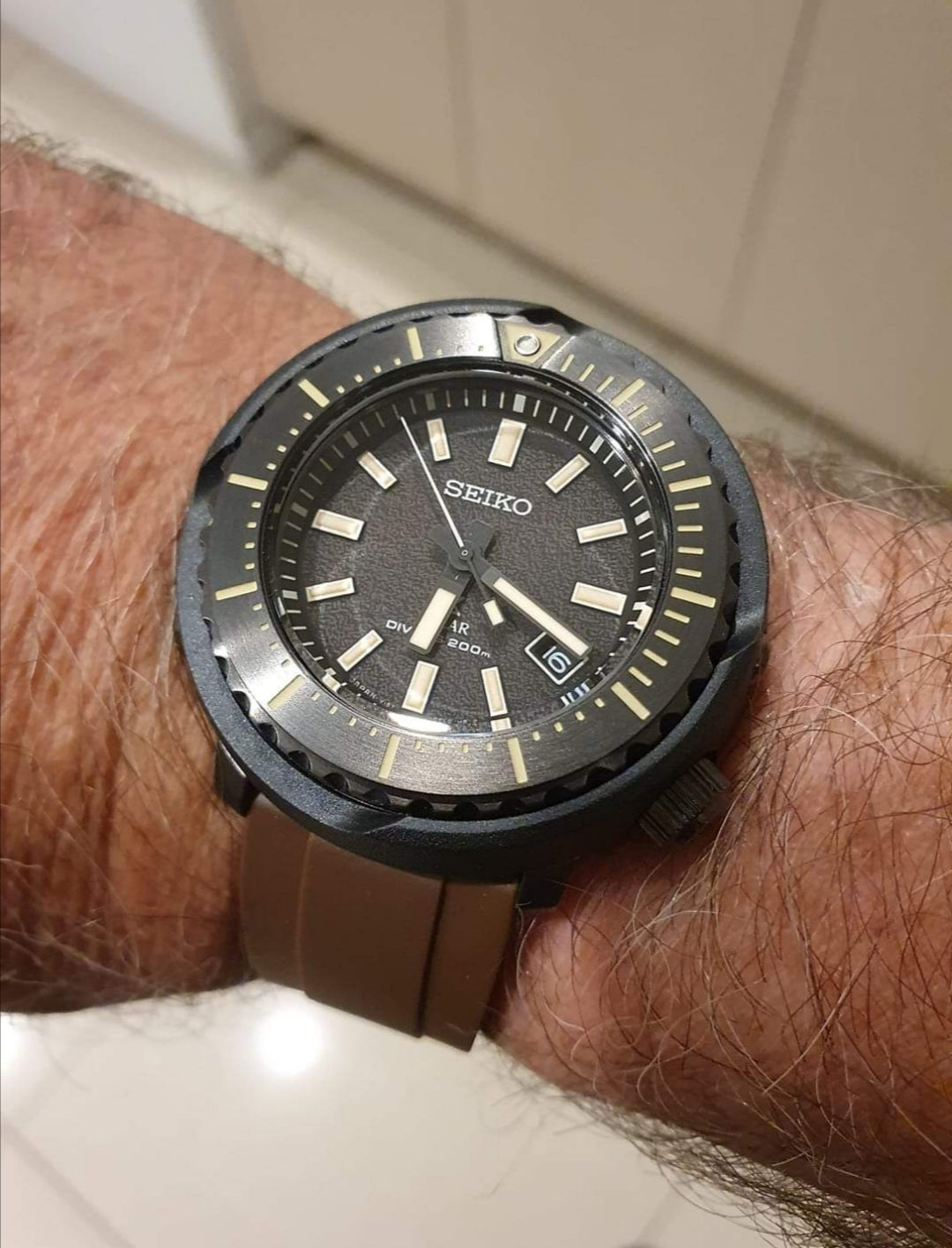 Seiko dive watch with black dial, luminous hour markers, date window, and brown rubber strap worn on wrist