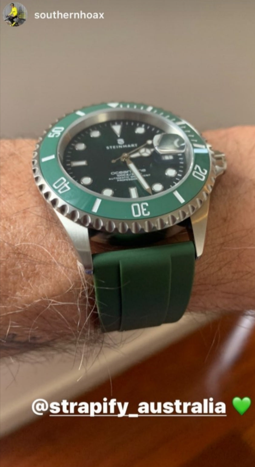 Stainless steel dive watch with green bezel and black dial worn on wrist with forest green rubber strap