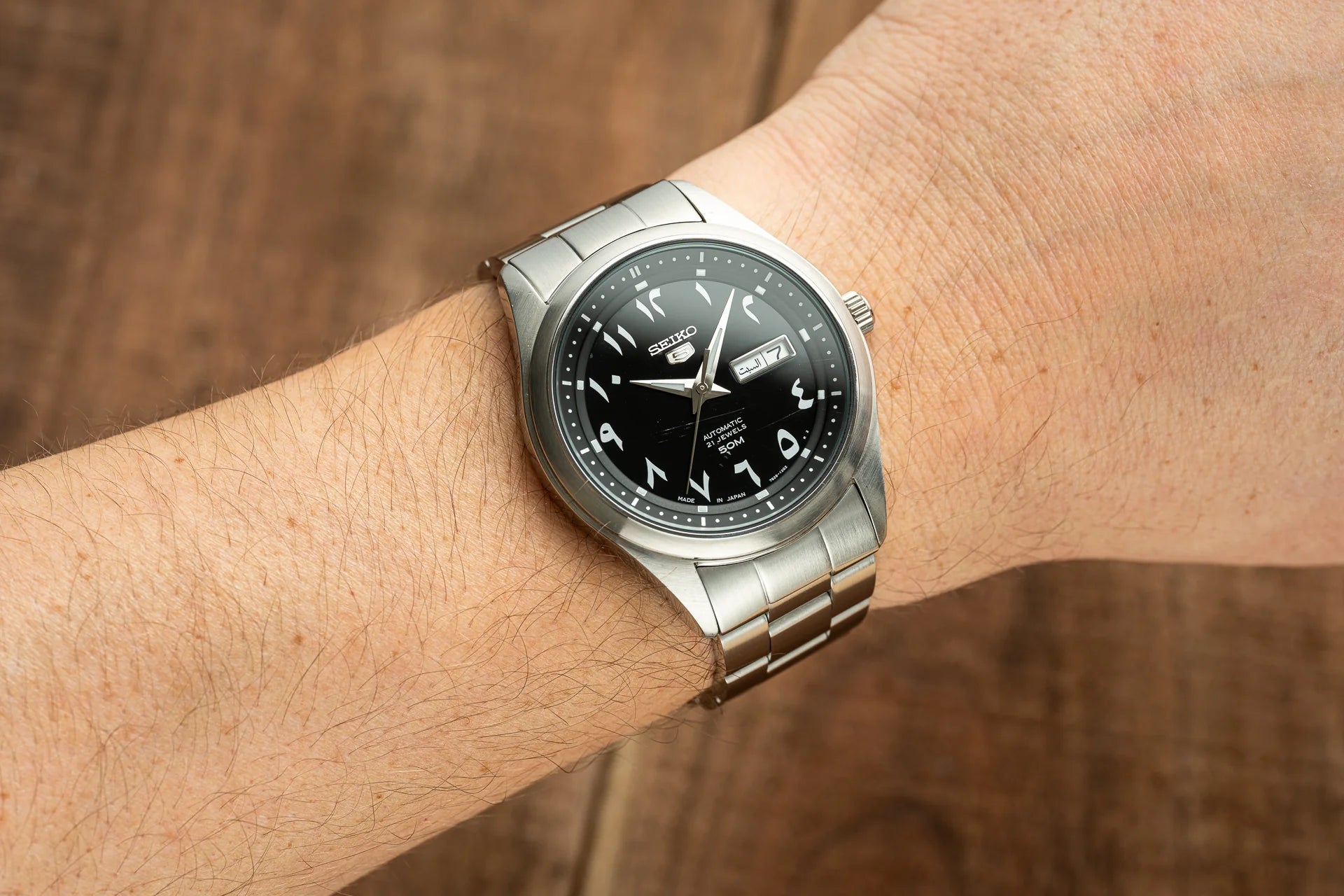 Seiko 5 automatic watch with Arabic numerals on black dial, stainless steel bracelet, worn on wrist