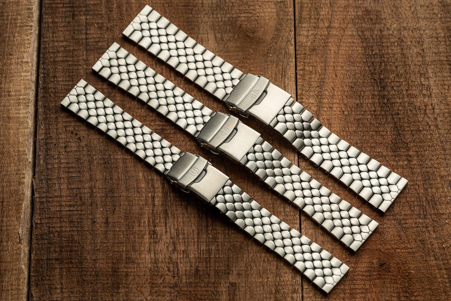 Three white snakeskin-textured watch bands with metal fold-over clasps, displayed in diagonal rows on wood background