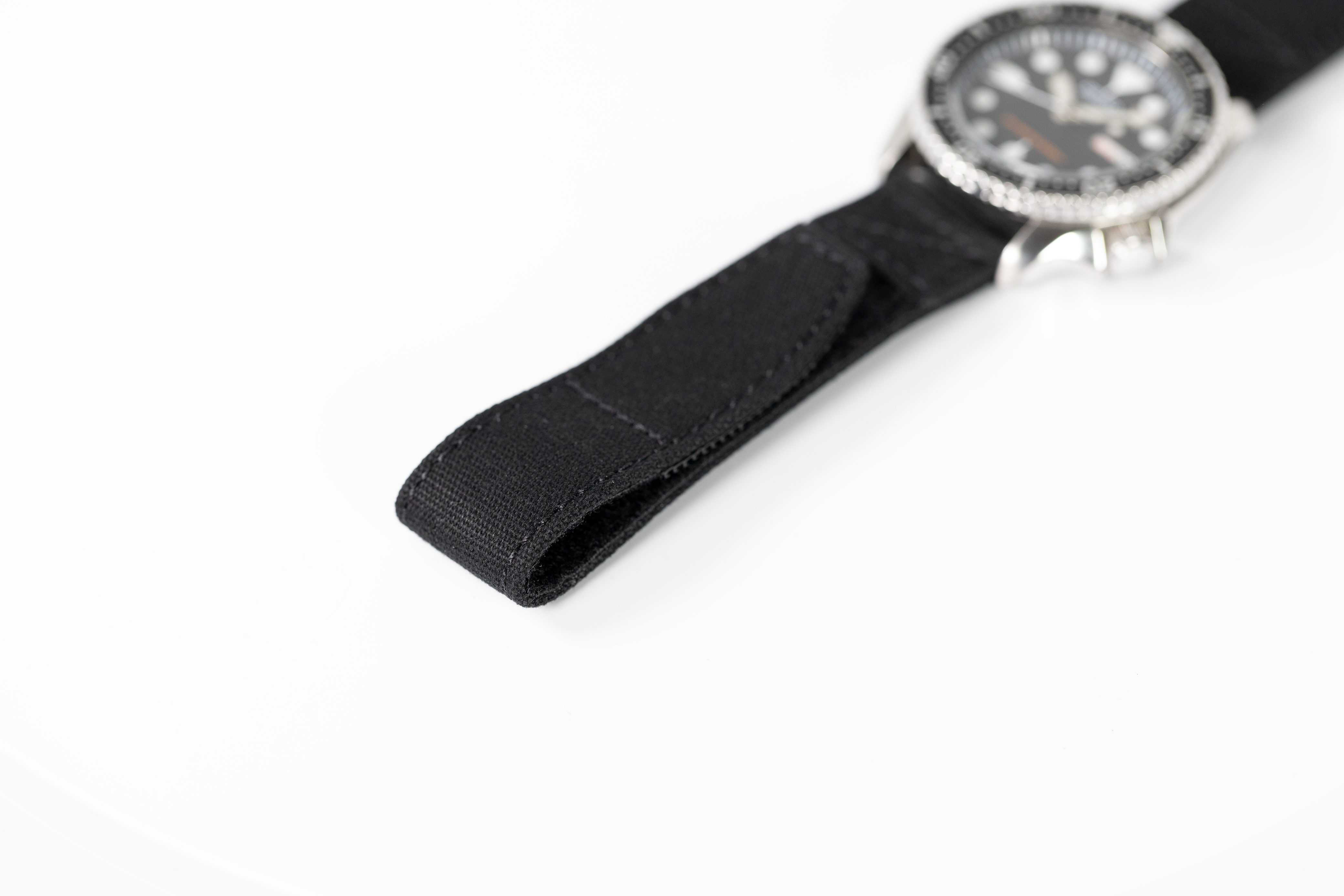Silver-case military watch with rotating bezel and black fabric quick-release velcro strap on white background