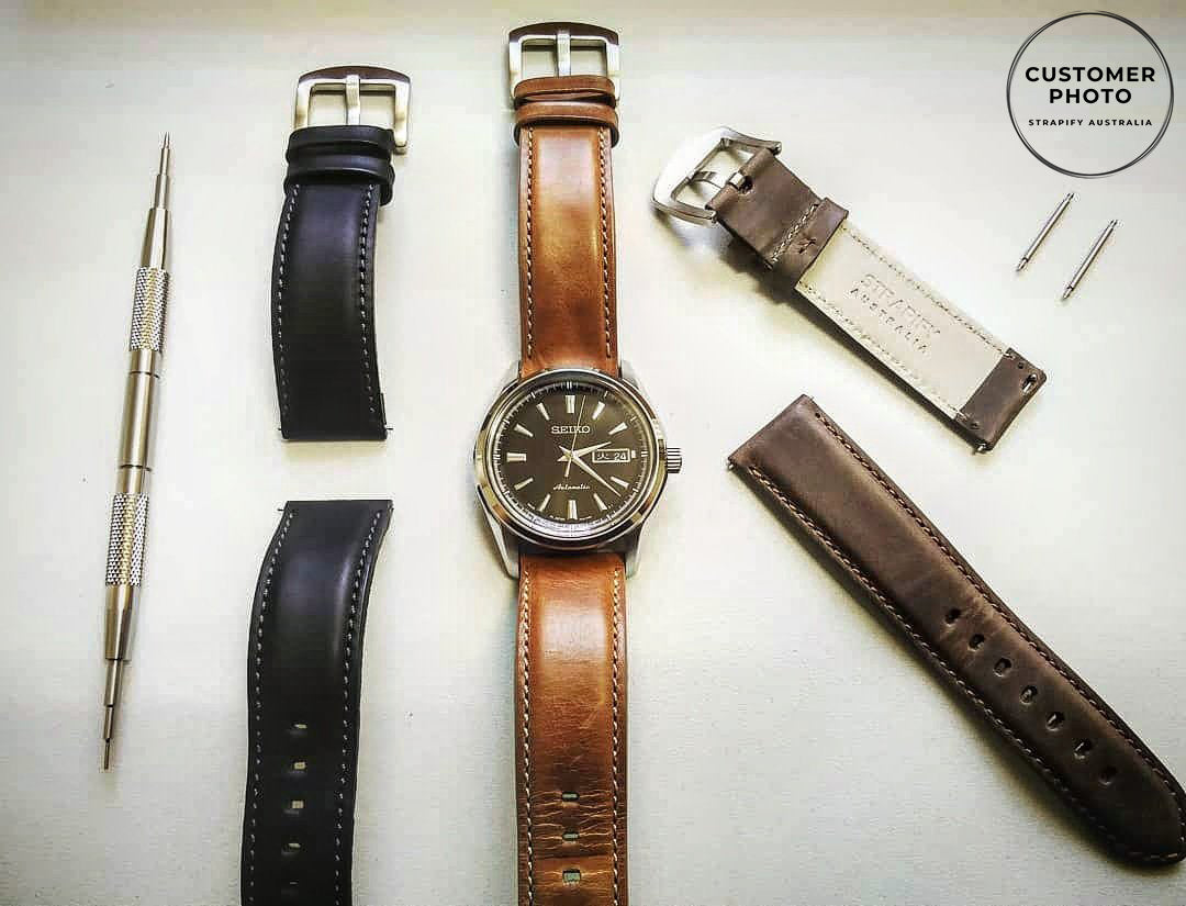 Brown padded leather quick release watch strap with stainless steel buckle, displayed with black strap and watch tool accessories