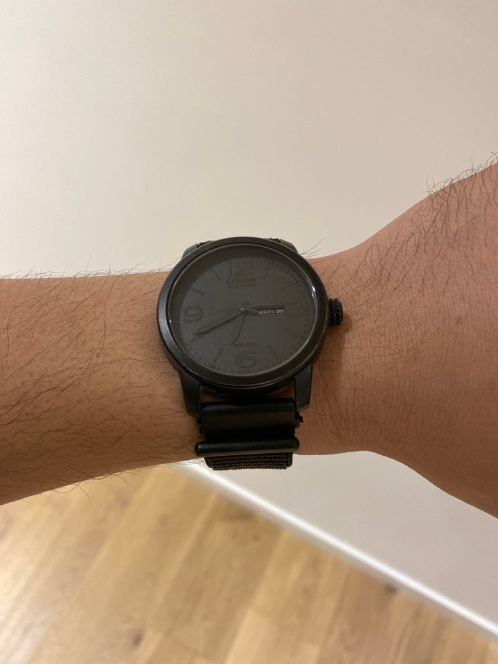 Black minimalist sports watch with velcro quick release loop strap worn on wrist, showing adjustable mesh band design