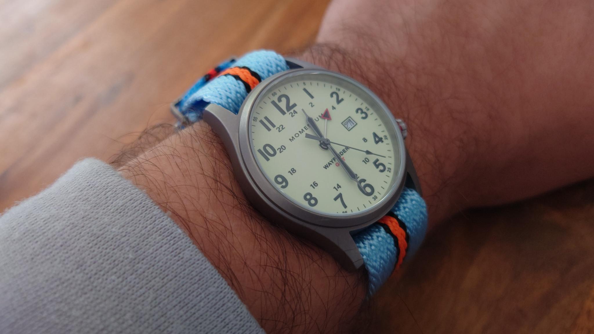 Men's watch with cream dial and blue orange striped fabric band worn on wrist