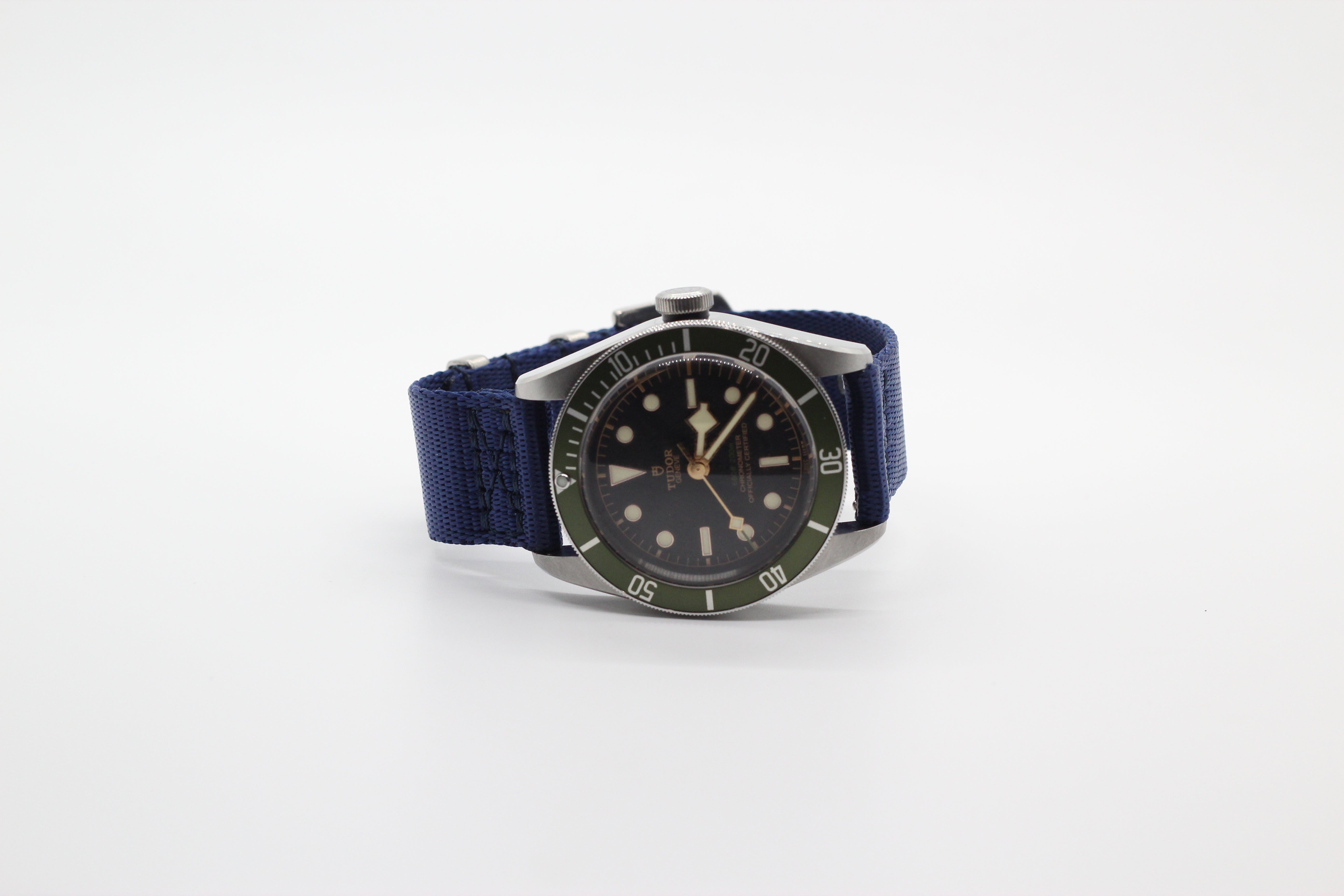 Vintage-style dive watch with black dial, green bezel, luminous hour markers, and navy blue fabric strap